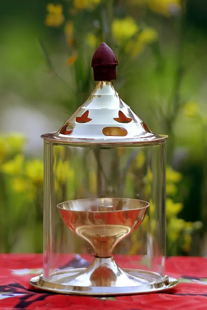 Brass diya under a glass cover with a decorated brass lid on a red cloth