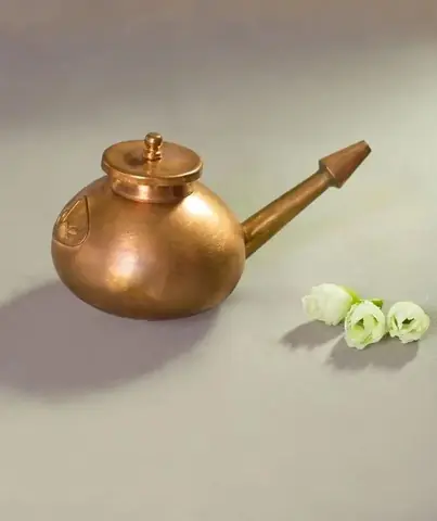 Neti pot on a grey ground beside small white flowers