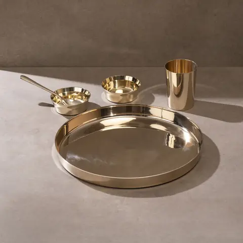 One kansa plate with bowls, glass and spoon on a grey ground