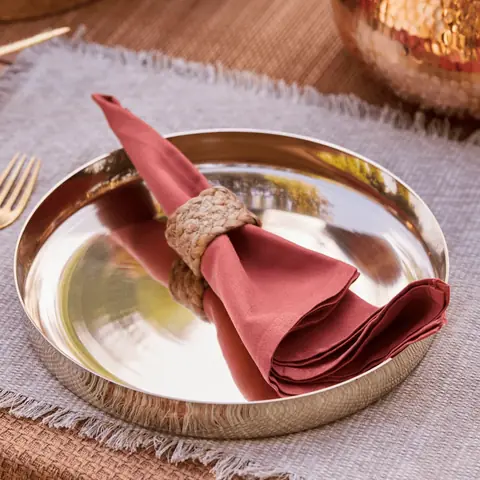 A kansa place setting on an orange cloth in front of a red gift box