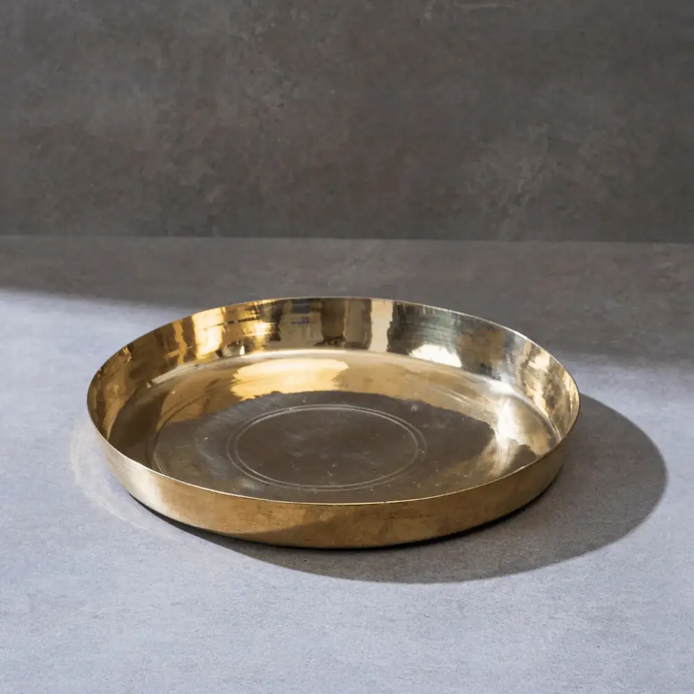 Kansa thaali plate on a grey ground, seen at an angle