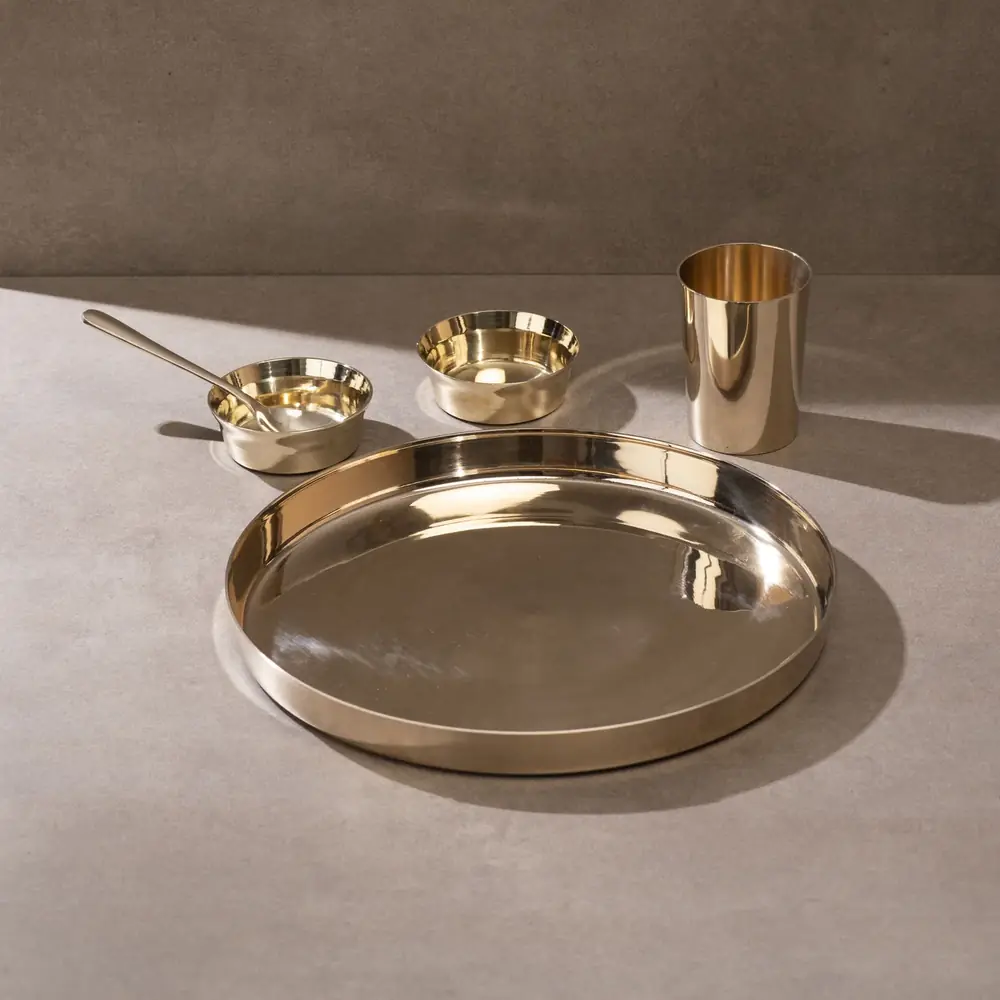 Kansa thaali with two bowls, a glass and a spoon on a grey ground