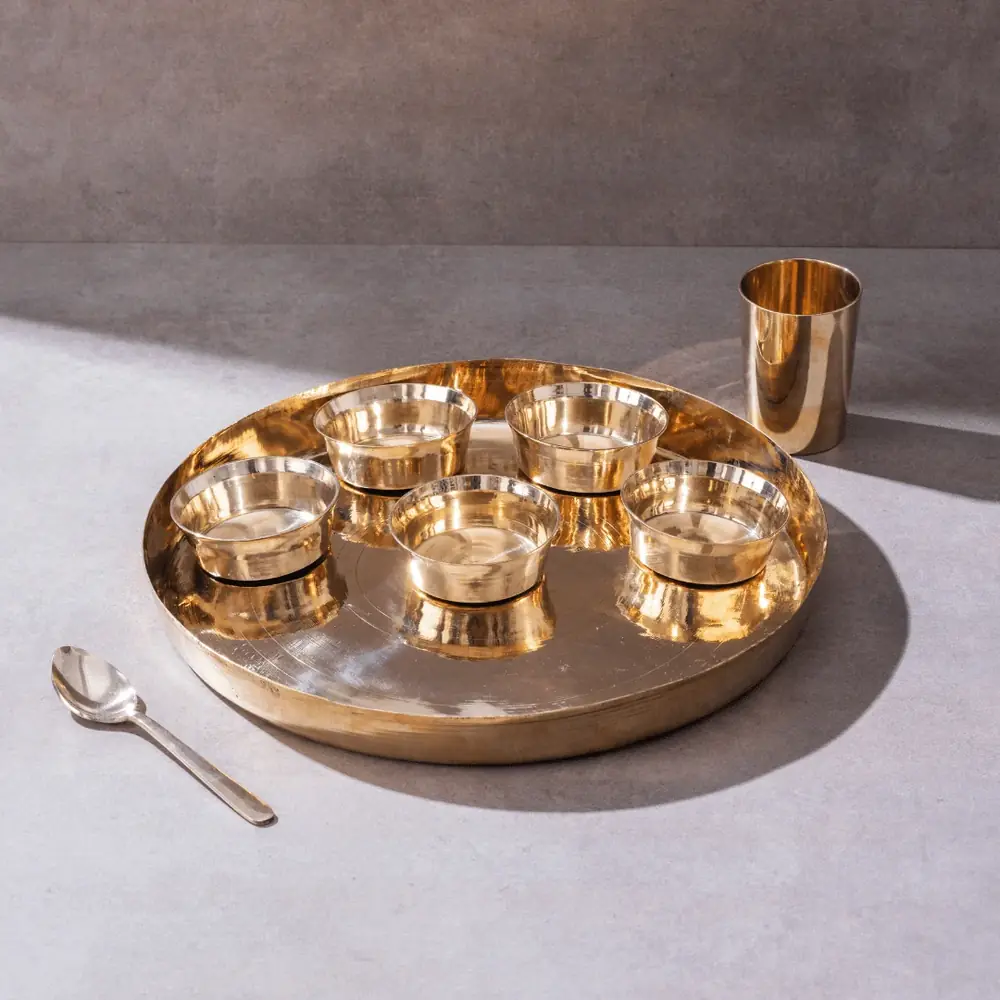 Kansa thaali with bowls, a glass and a spoon on a grey ground
