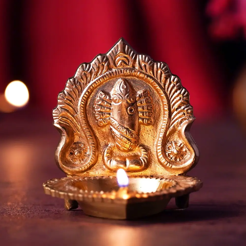Brass oil lamp with a carved Devi and serpent in an arch, lit