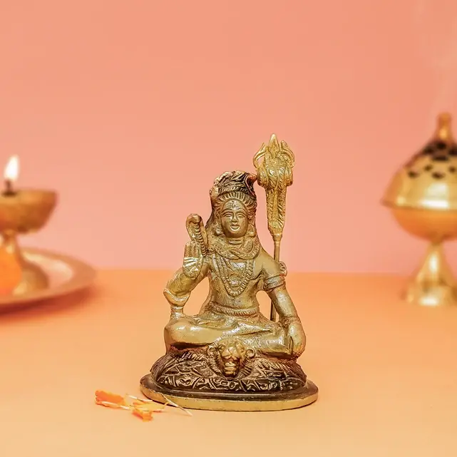 Seated brass Shiva with a trident on a peach ground