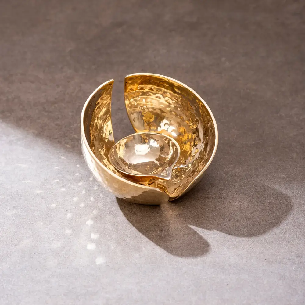 Hammered golden brass lotus diya on a grey ground