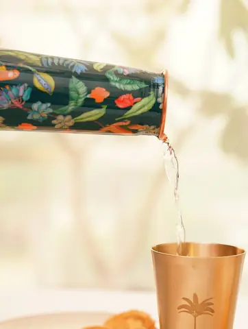 Water being poured from the bottle into a copper tumbler