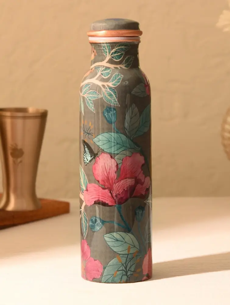 Grey copper bottle with pink flowers and leaves on a table