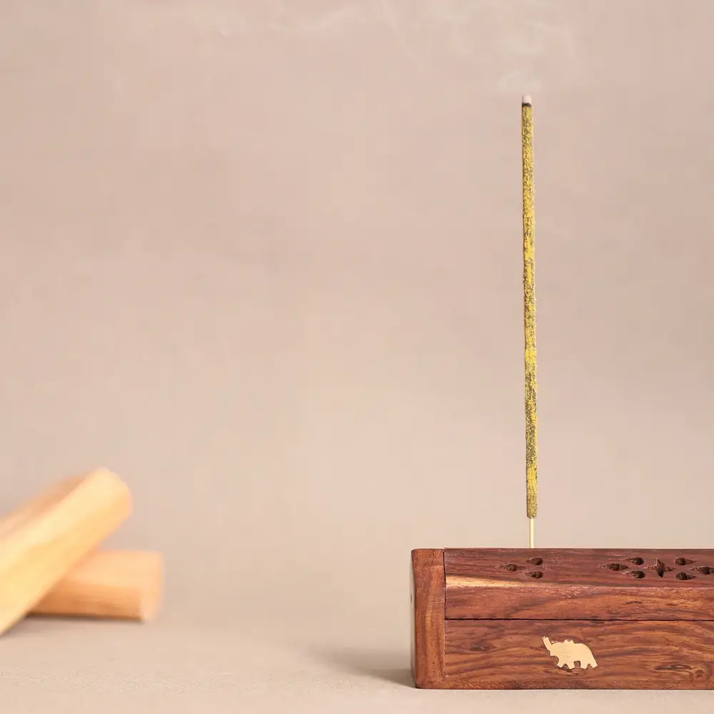 A lit stick in a small wooden holder beside a piece of sandalwood
