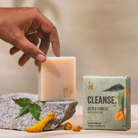 A hand holding the cream soap bar beside the green box