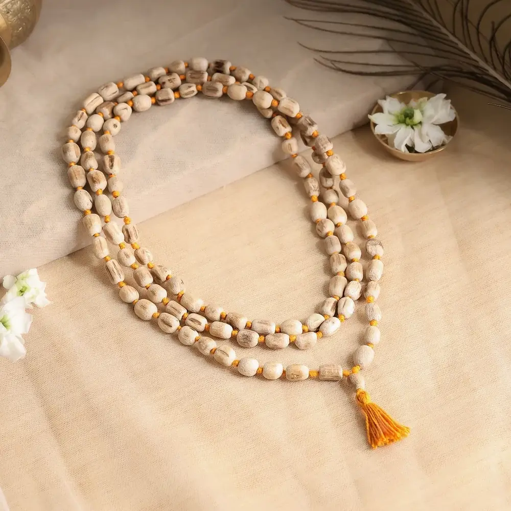 Tulsi wood mala with an orange tassel coiled on a cream cloth