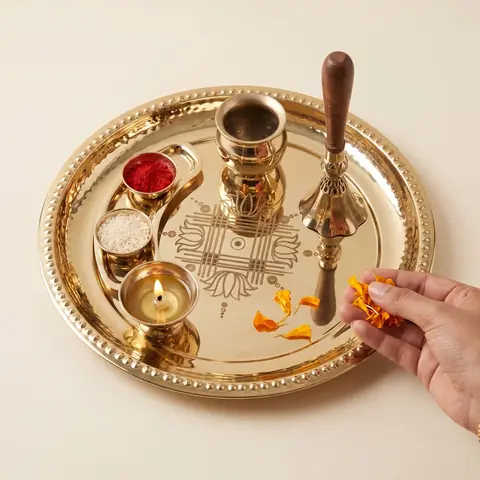 Hand placing a marigold petal on the thaali beside the diya, bell and bowls