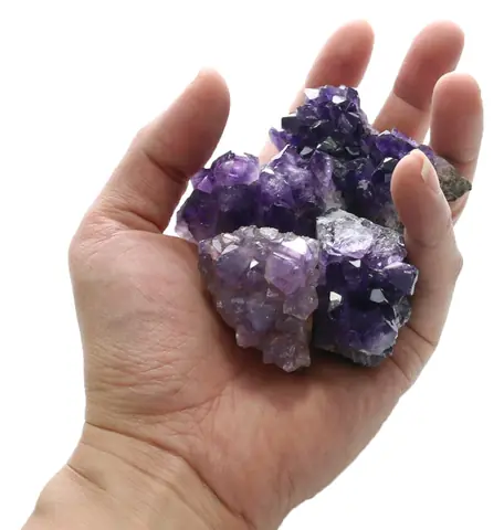 A hand holding a small amethyst cluster for scale
