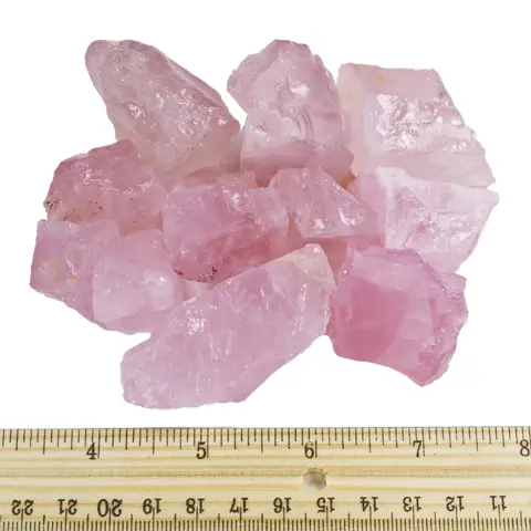 Raw rose quartz pieces beside a ruler for scale