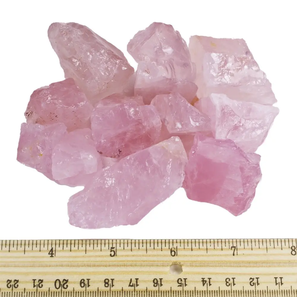 Raw rose quartz pieces beside a ruler for scale
