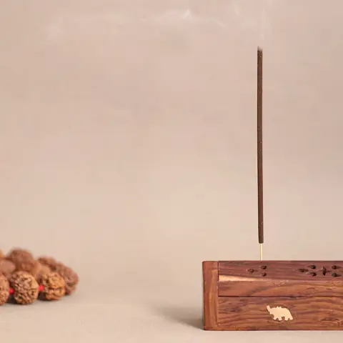 A single stick burning in a small wooden holder beside rudraksha beads