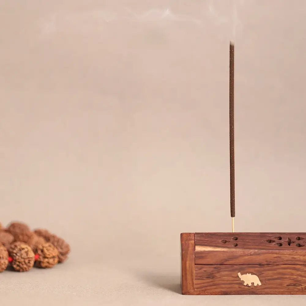 A single stick burning in a small wooden holder beside rudraksha beads
