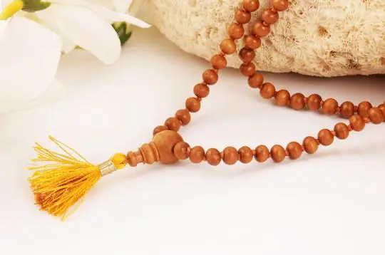 Sandalwood mala with a yellow tassel on a pale ground