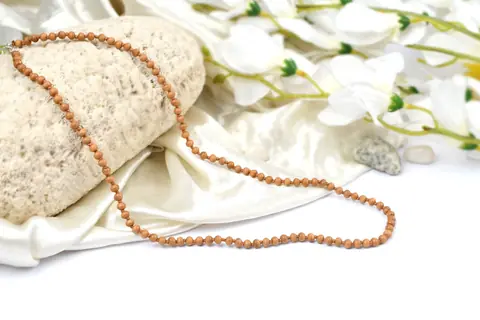 Sandalwood mala beside a cloth bag on a stone