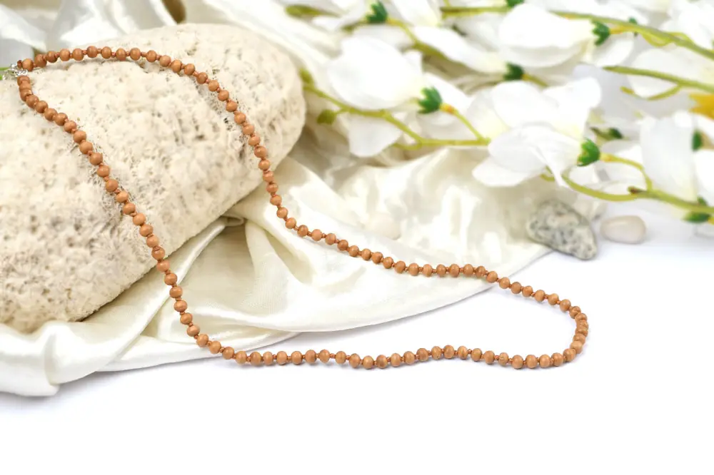 Sandalwood mala beside a cloth bag on a stone