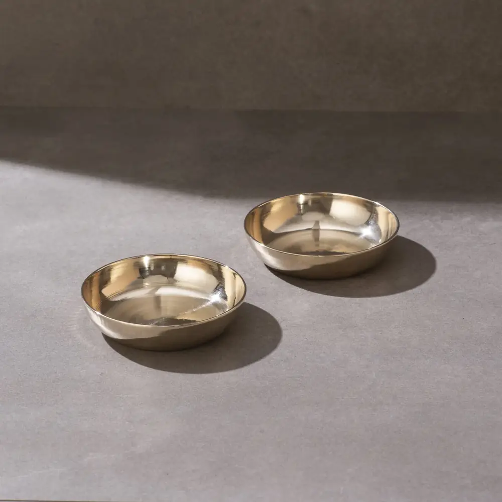 Two kansa flat dish bowls on a grey ground