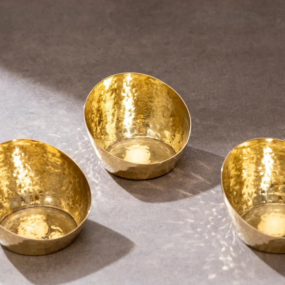 Two hammered brass tea light holders on a stone surface
