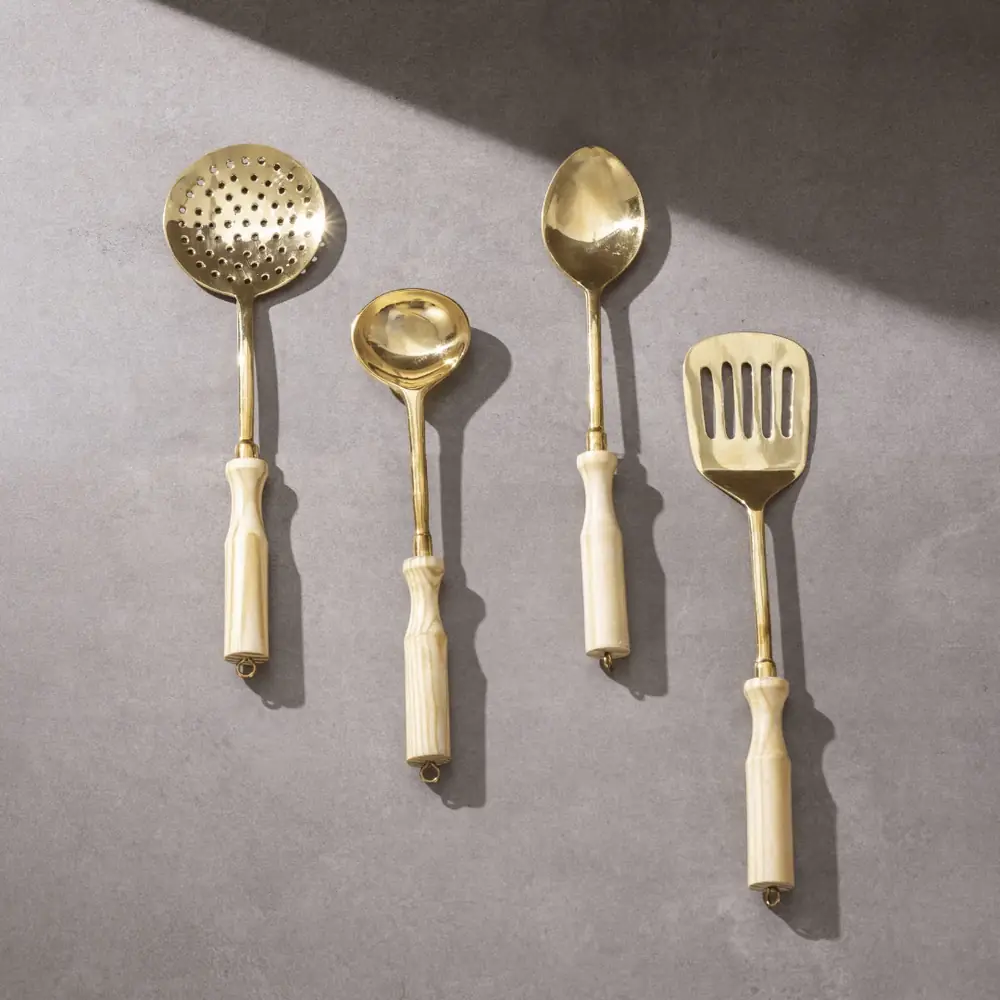 Brass ladle set with wooden handles on a pink stand beside maroon boxes
