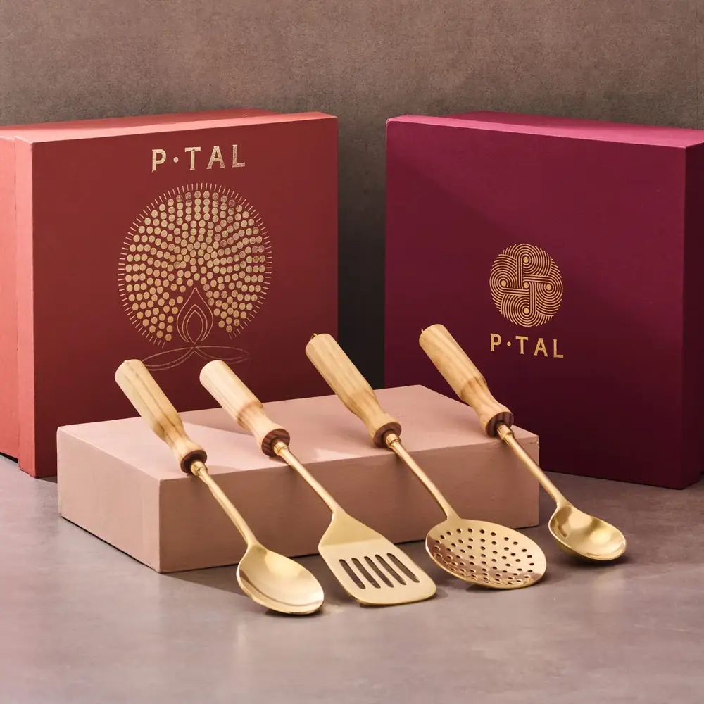 Four brass kitchen tools with wooden handles on a grey ground