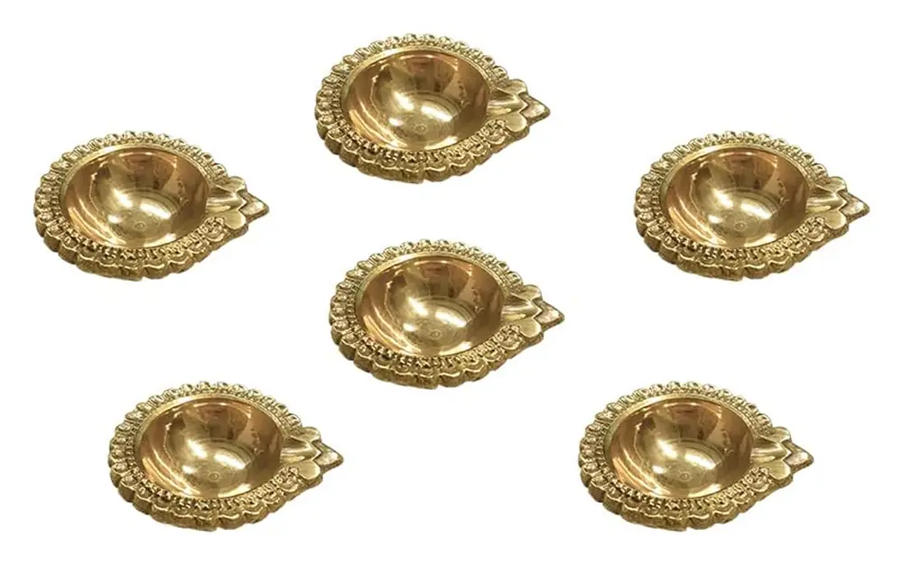 Six brass diyas laid out on a white ground