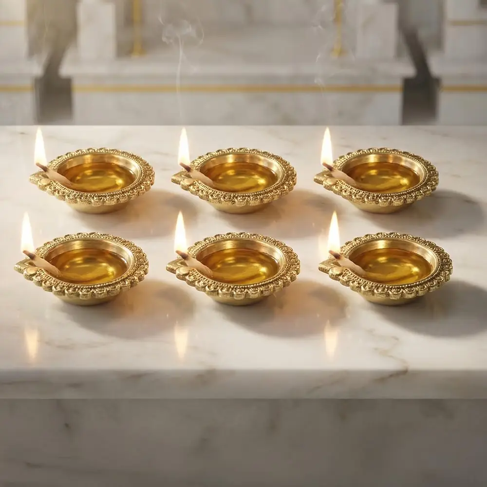 Six lit brass diyas on white marble