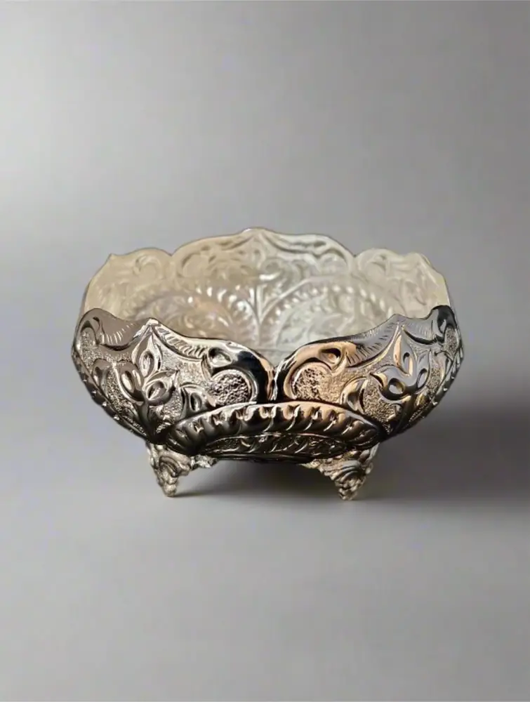 Silver-tone brass urli on three feet on a wooden table