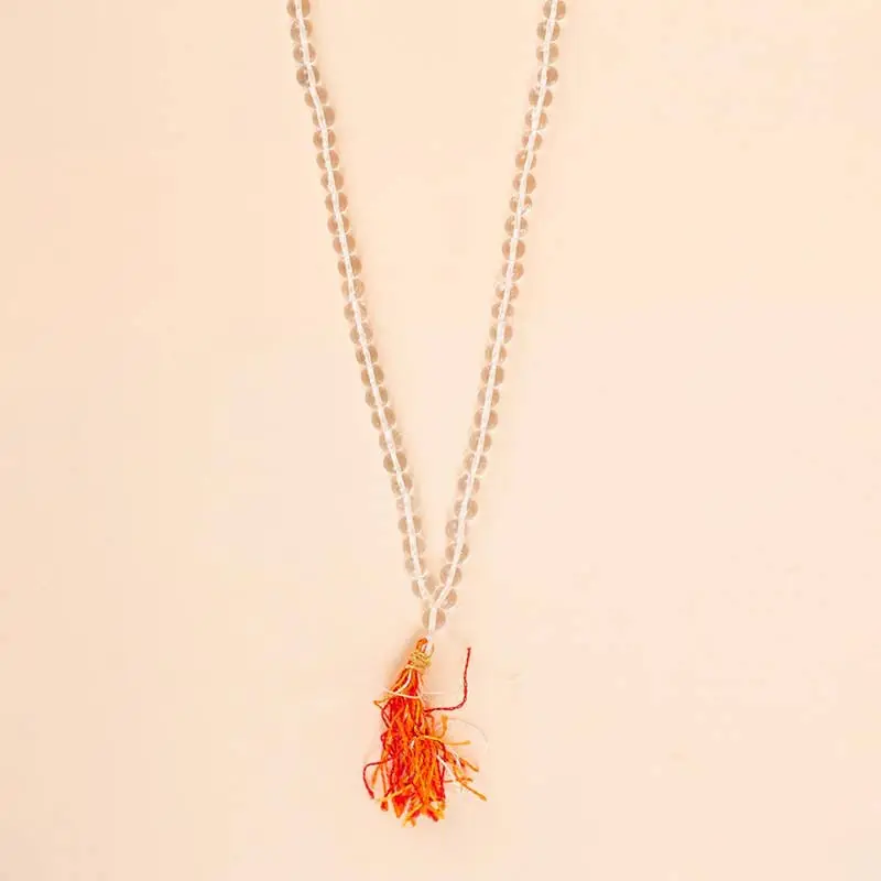 Pale quartz mala with a red and orange tassel on a peach ground