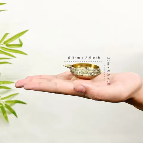 A small brass diya held in the palm of a hand, 6.3 cm marked
