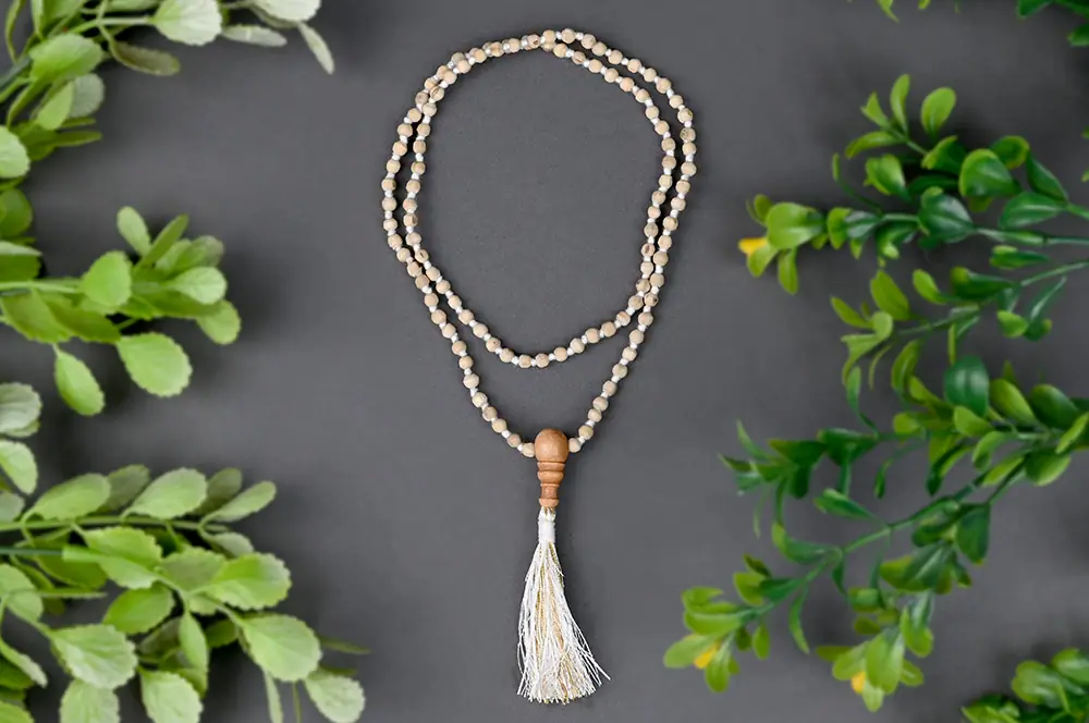 White tulsi mala with a silver tassel among green leaves