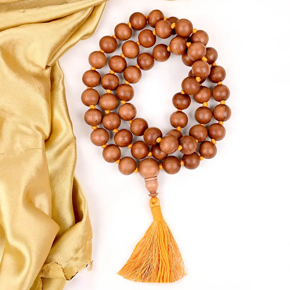 Brown sandalwood mala coiled on yellow cloth with an orange tassel