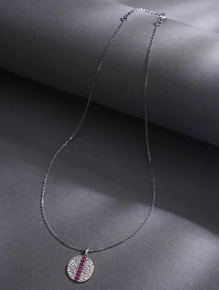 Silver chain with round pendant laid on dark grey cloth
