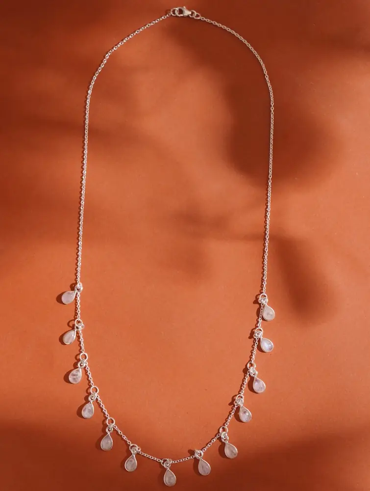 Silver necklace with small pale drops laid on a rust coloured ground