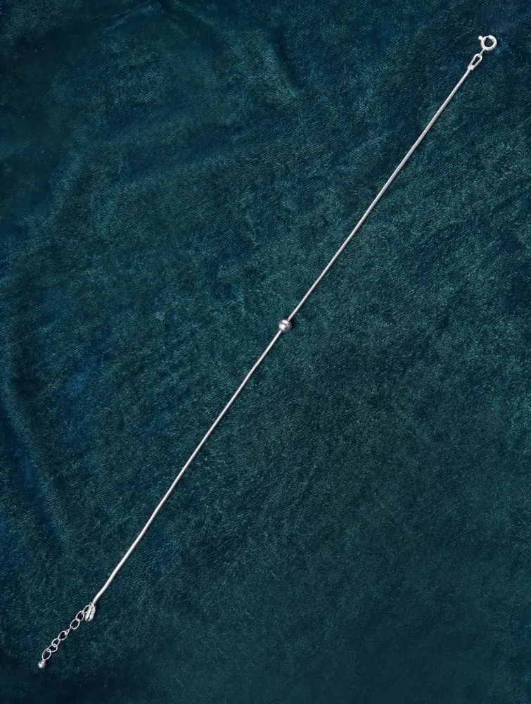 Silver anklet laid out flat on dark teal cloth
