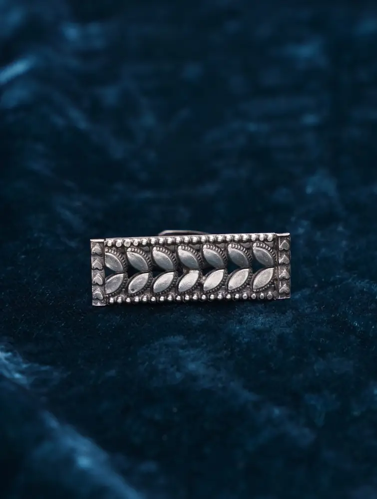 Silver ring with a leaf patterned rectangular top on dark blue cloth
