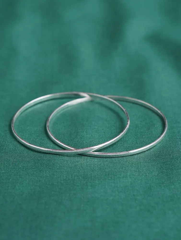 Two slim silver bangles lying on green cloth