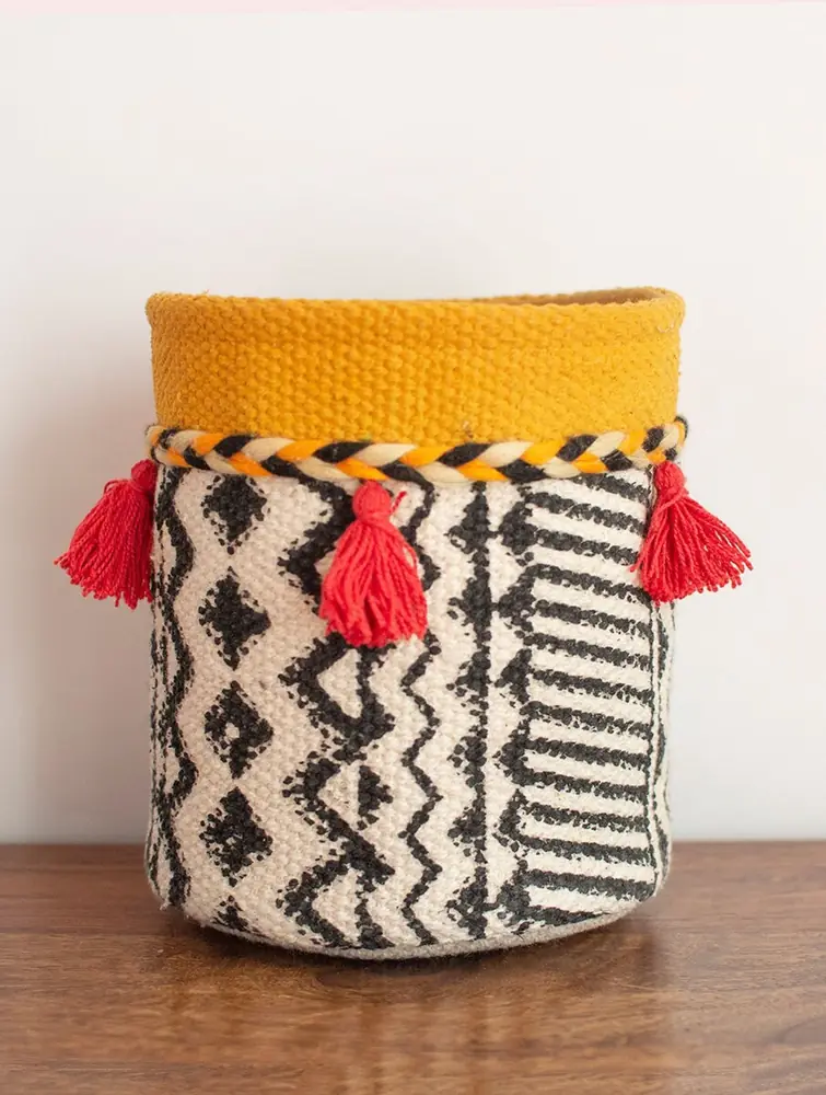 Yellow canvas planter with red tassels on a wooden surface